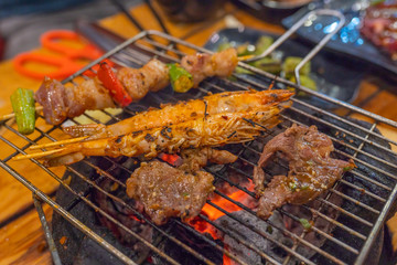 Meat slices, pork kebab and shrimp on flaming charcoal stove