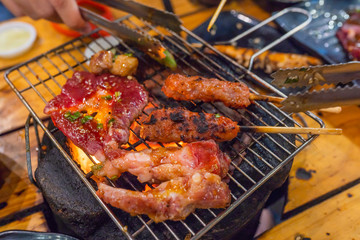 Human using grilling tongs picking skewer on barbecue charcoal stove