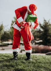 Obraz premium Stock photo of Santa Claus without beard standing putting presents in a red bag. Christmas time