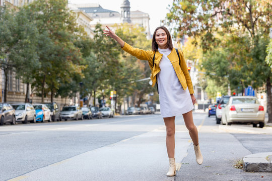 Young Woman Hailing A Taxi Ride. Beautiful Charming Woman Hailing A Taxi Cab In The Street. Businesswoman Trying To Hail A Cab In The City. Tourist Woman Hailing A Taxi