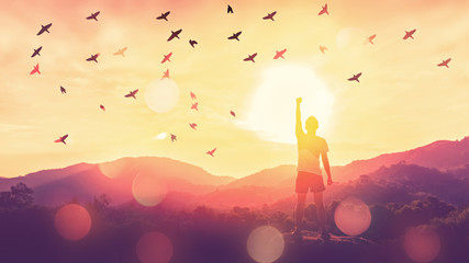 Freedom feel good and travel adventure concept. Copy space of silhouette man rising hands on sunset sky at top of mountain and bird fly abstract background.