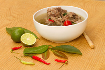 Hot and spicy soup with Cha Muang ribs In a white cup on a wooden table.