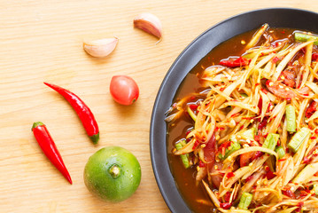 Som Tam or Spicy Papaya Salad In a black plate on a wooden table.