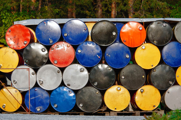 Fototapeta premium Warehouse of industrial waste in the yard. Oil, petrol drums or chemical barrels stacked up. Waste of colored tank oil. Environmental pollution by improper storage of danger materials.