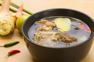 Spicy & Sour Soup with Chicken and young tamarind leaf In a white cup on a wooden table.