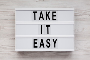 'Take it easy' words on a lightbox on a white wooden surface, top view. Overhead, from above, flat lay.