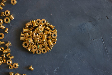 Round form made of gold pop rivet nuts ond lochnuts on black tectured chalk board surface. Close up. Horizontal with copy space. Fasteners, screws and details. Top view