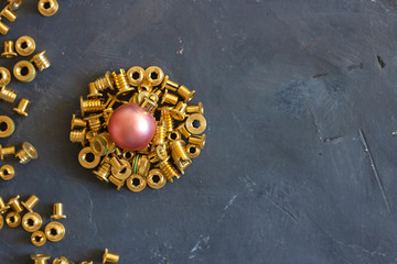 Round form made of gold pop rivet nuts ond lochnuts with pink christmas ball on it on black tectured chalk board. Horizontal copy space. Fasteners, screws and details. Top view. New year concept.