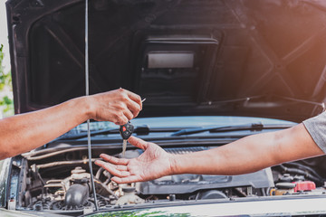 Closeup at the hands of the mechanic is returning the keys to the customers who have repaired the car in the garage after the repairs are done, transportation and insurance industry concepts.