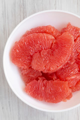 Red grapefruit slices in a white bowl on a white wooden surface, top view. Flat lay, overhead, from above. Close-up.