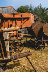Historische Dreschmaschine mit anschließender Strohpresse in Betrieb. Im Vordergrund steht ein historischer Wagen aus Holz für den gemähten Weizen