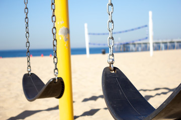 A swing set playground on the beach, featuring a volleyball net and the ocean in the background