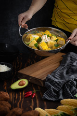 A person serving chicken soup with potato and corn