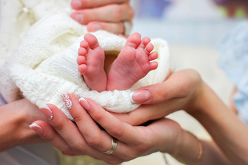 Mom and dad hands hold small legs of their newborn baby, wrapped in a white warm blanket