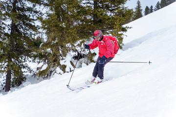 Fototapeta na wymiar Side image of sports man in red jacket and with backpack skiing in winter resort