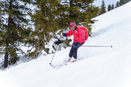 Side image of sports man in red jacket and with backpack skiing in winter resort