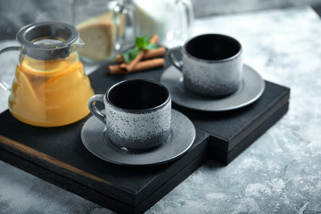 Transparent glass teapot with chitrus tea and cups, tea set on a wooden table. Close up, gray background, soft light.
