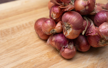 Close up of organic raw shallots on bamboo chopping block on brown wooden floor background