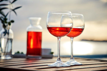 two glasses of rose wine with  olives against blue water on a pier..