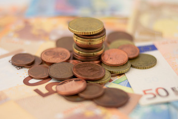 Many scattered euro coins and a column on a background of fifty and 20 euro bills
