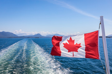 A close up of the Canadian flag flying in the wind at the back of ferry as the boat makes it way through the Inside Passage, British Columbia, Canada