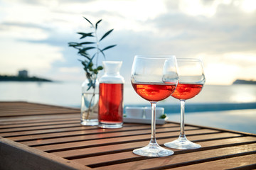 two glasses of rose wine with  olives against blue water on a pier..