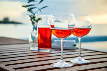 two glasses of rose wine with  olives against blue water on a pier..