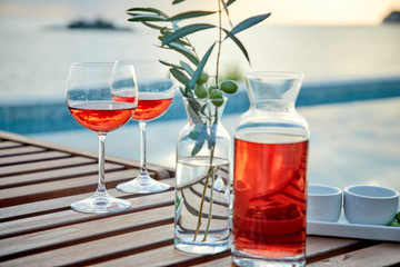 two glasses of rose wine with  olives against blue water on a pier..