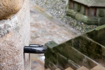 Shallow focus of a metal handrail seen attached to the outside perimeter of a historical building.  The steps lead to a boundary wall.