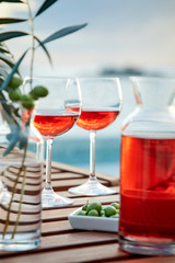 two glasses of rose wine with  olives against blue water on a pier..