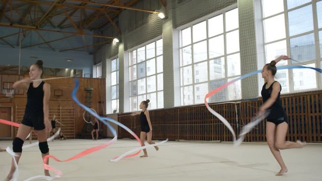 Group of young teenage girls in sportswear practicing gymnastics with colorful ribbons together in school gym