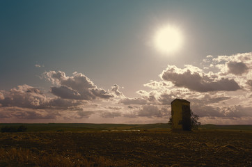 Sun in a cloudy sky over a tall concrete stand in open field
