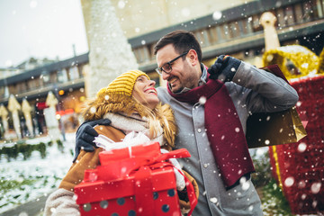 Young couple dressed in winter clothing holding gift boxes outdoor.