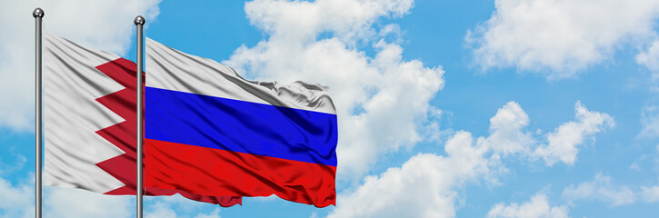 Bahrain and Russia flag waving in the wind against white cloudy blue sky together. Diplomacy concept, international relations.