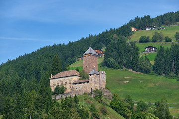 Fototapeta na wymiar Aerial view of the castle in the Alps surrounded by meadows, forests and mountains. Castle on a hill. Flying on drone.
