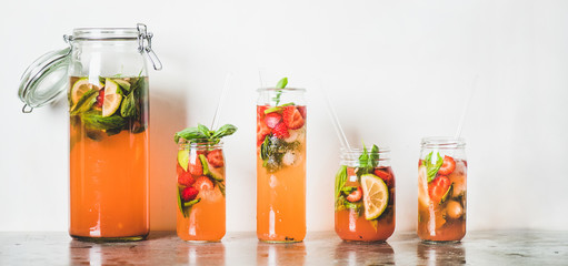 Homemade strawberry and basil lemonade or ice tea in glass tumblers with eco-friendly plastic-free straws on grey concrete table, white wall at background, copy space, wide composition