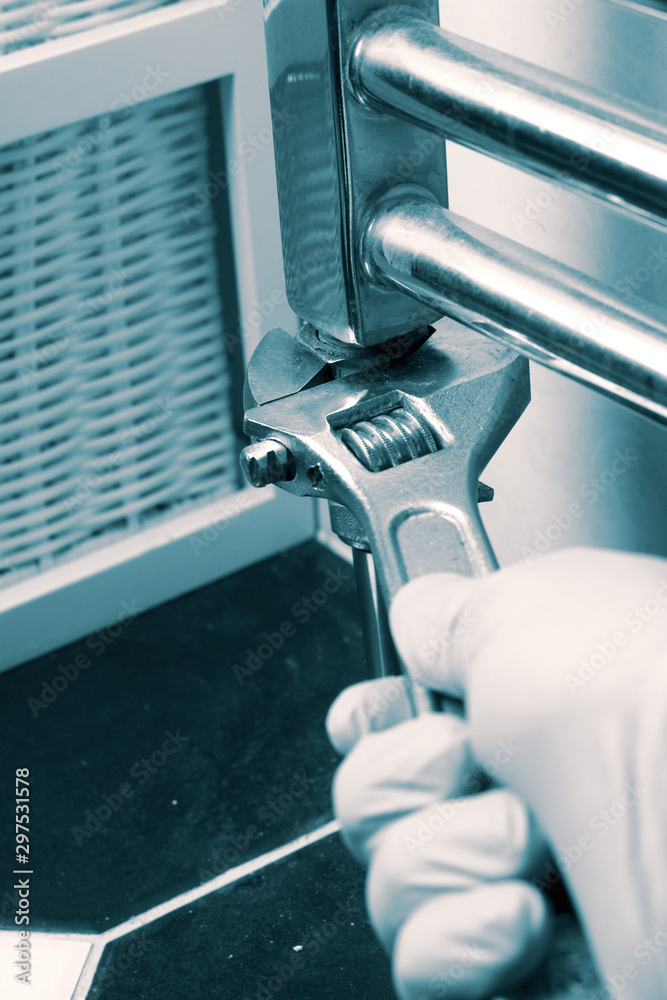 Wall mural man installing tightening a nut with a spanner wrench on a modern wall mounted radiator in a bathroo