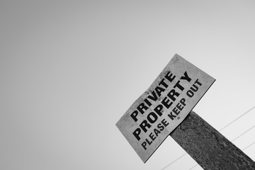 Monochrome view of a Private Property sign seen attached to a wooden post at the entrance to a private land in a rural location.