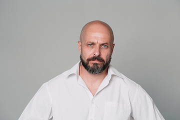 Handsome serious middle-aged man in a white shirt looks seriously at the camera on a gray background with copy space