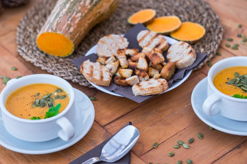 Rustic table with a raw pumpink in the middle of  it. Healthy eating in autumn and winter time. Wooden table with two bowls of pumpkin cream soup.