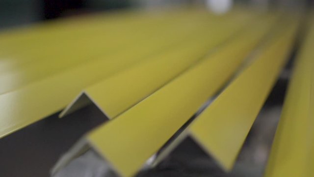 Multiple identical L-Profile bar left on table to dry after being freshly painted with a bright yellow coating. Slow motion. 