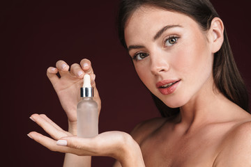 Image of half-naked woman holding serum bottle and looking at camera