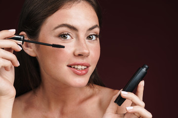 Image of pleased half-naked woman looking at camera and using mascara