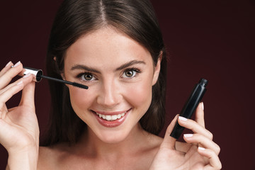 Image of smiling half-naked woman looking at camera and using mascara