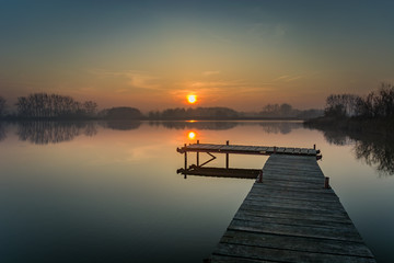 Obraz premium Wooden jetty on a calm lake, evening sky and sunset