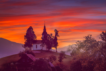 A beautiful shot of a silhouette of a church in the misty Alpine mountains with orange sunset sky in the background. Great for desktop wallpaper and backgrounds