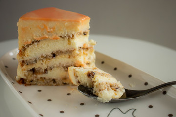 A piece of orange mirror glazed cake with cream cheese filling and nuts on white plate.