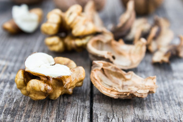Peeled walnuts and walnut kernels lie on a rustic old wooden table.