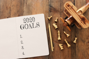 Business concept of top view 2020 goals list with notebook, chess figures and old plane toy over wooden desk