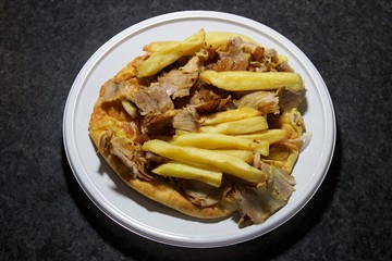 Pita gyros Greek food of pitta bread pork meat vegetables french fries mustard and ketchup sauce served on a white plate in a restaurant, on a dark marble table background